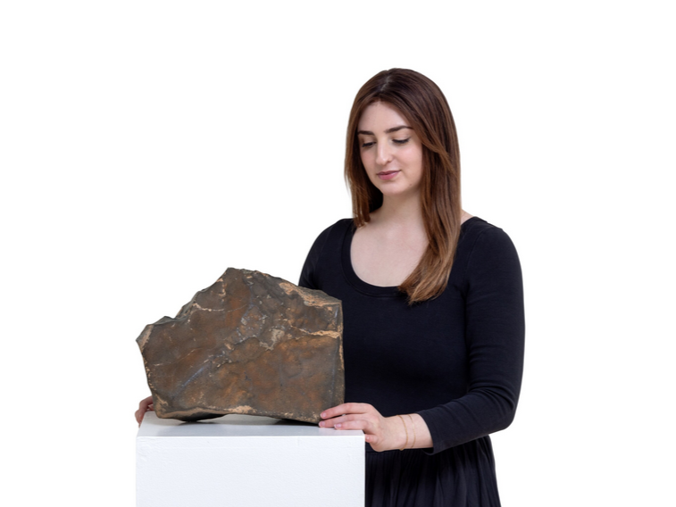 A woman at Sotheby’s stands beside the Martian meteorite NWA 16788 displayed on a pedestal before auction