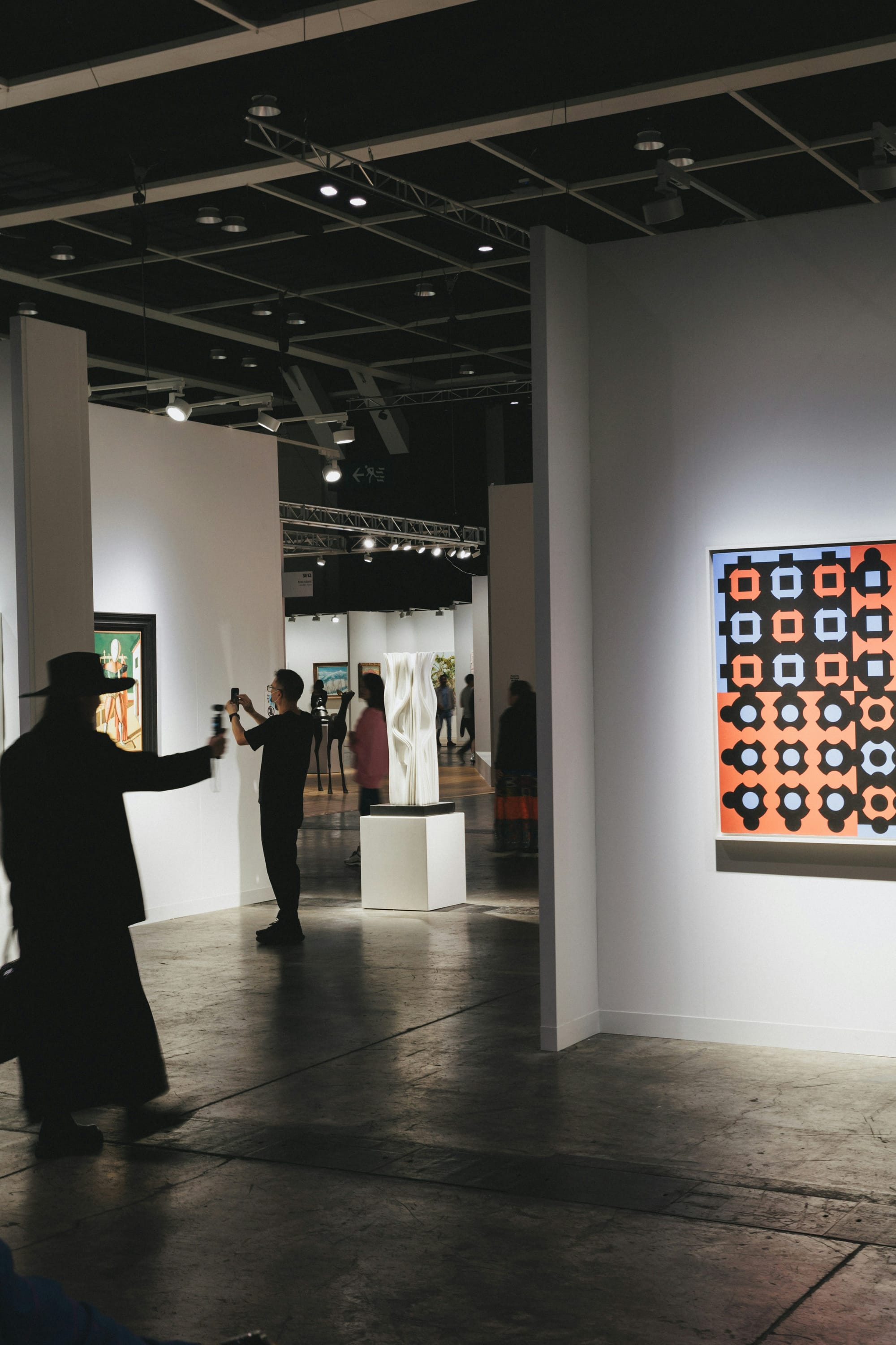Visitors walking through art fair aisles with booths under bright lights during uncertain market conditions