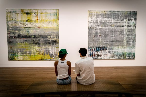 Two persons sitting thoughtfully in front of two large abstract modern artworks in a gallery