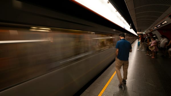 Timelapse photo of a train moving on rails beside a quiet pier with people standing still — symbolizing art, procrastination, and the contrast between motion and reflection.