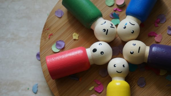 Six wooden figures with different facial expressions arranged in a circular formation on a wooden surface.