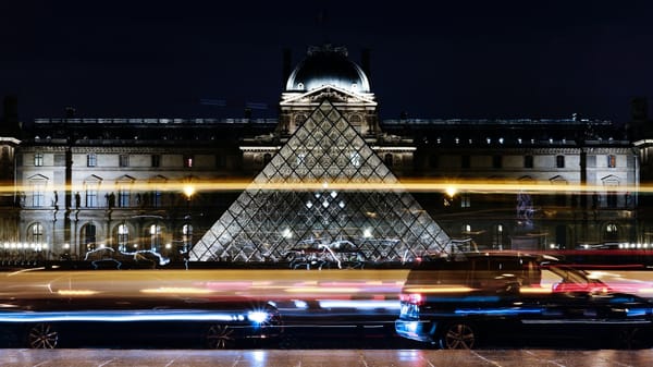 The Louvre Pyramid illuminated at night in Paris, symbolising the intersection of architecture and presidential legacy.