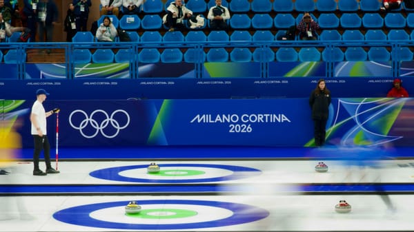 The curling venue during the Milano Cortina 2026 Winter Olympics, with athletes competing on the ice under arena lighting.